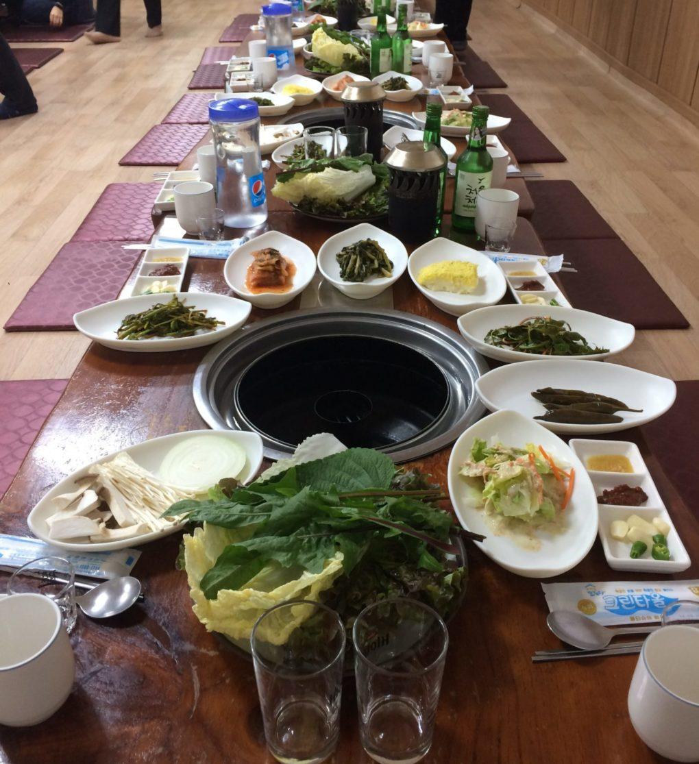 Various Korean foods and soju on a dinner table set.