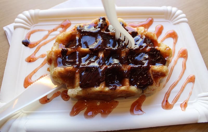 Waffles topped with cacao nibs and fresh strawberries, served on a white plate.