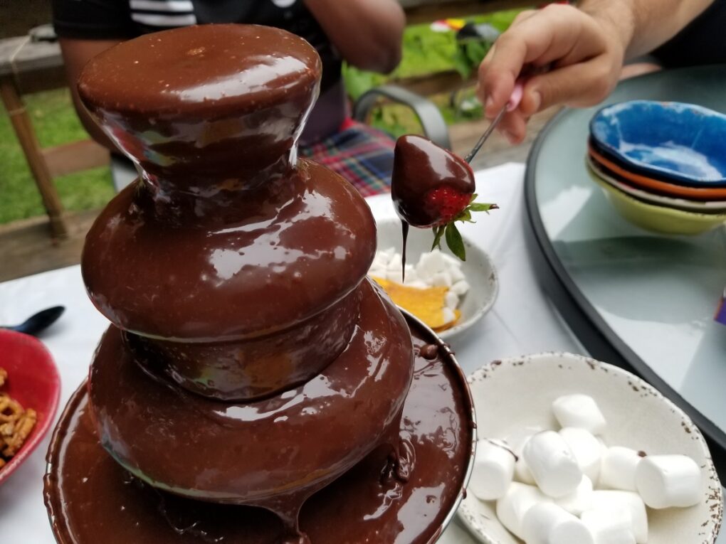 someone putting a strawberry into the melted chocolate in a chocolate fountain.
