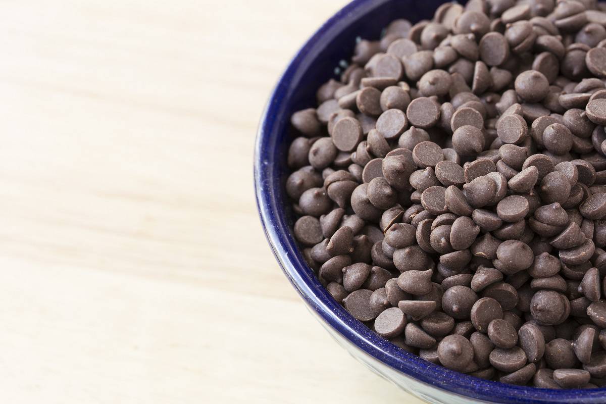 Chocolate chips in blue bowl close up with wooden patterning in the background.
