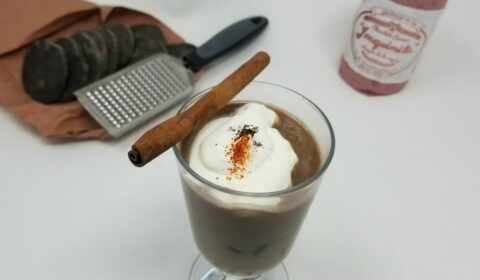 a cup of Mexican hot chocolate with whipped cream on top, red spice and cinnamon stick