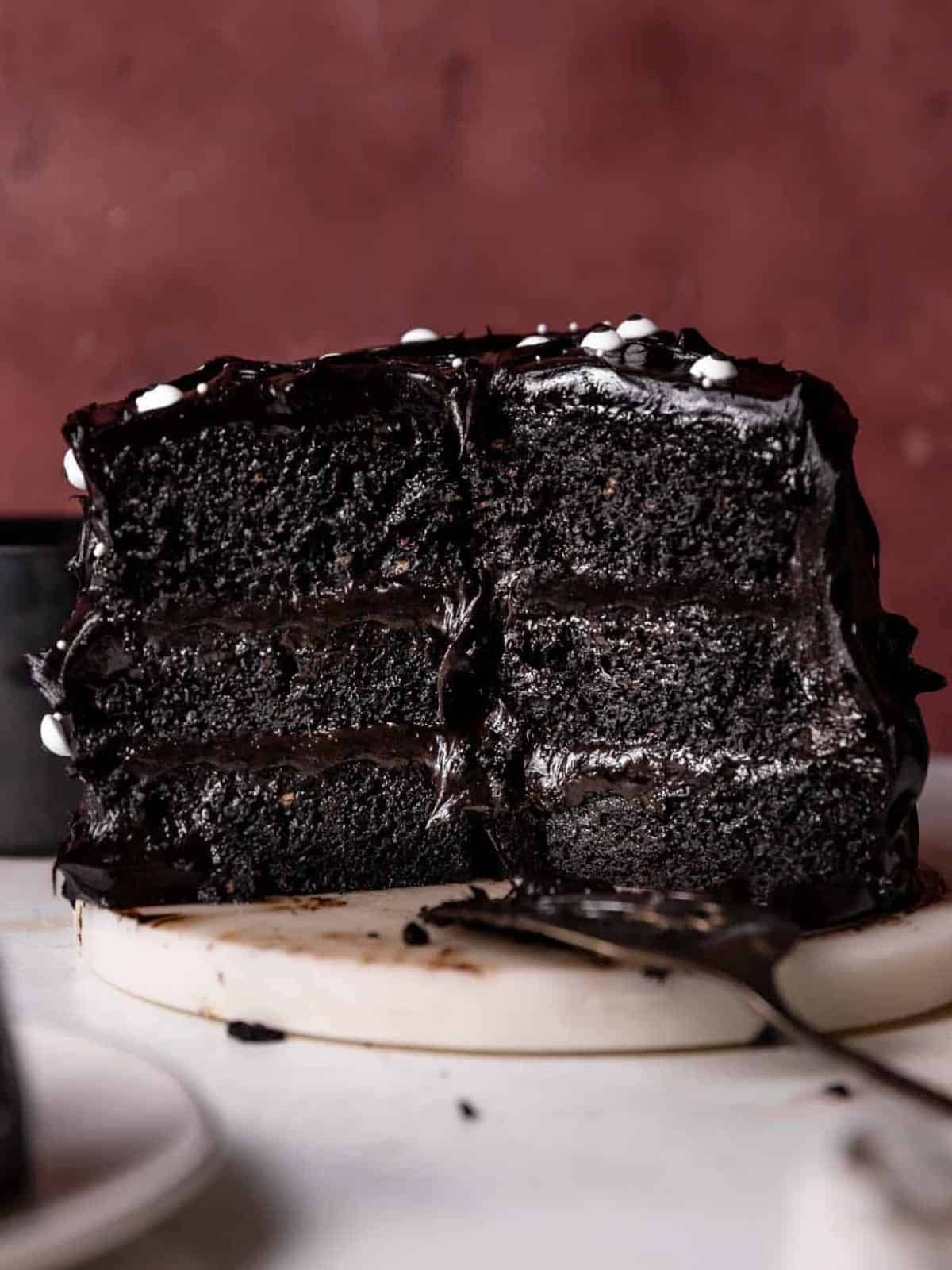 A slice of rich Black Velvet Cake on a plate, perfect for a Halloween celebration, with dark chocolate frosting and spooky decorations.