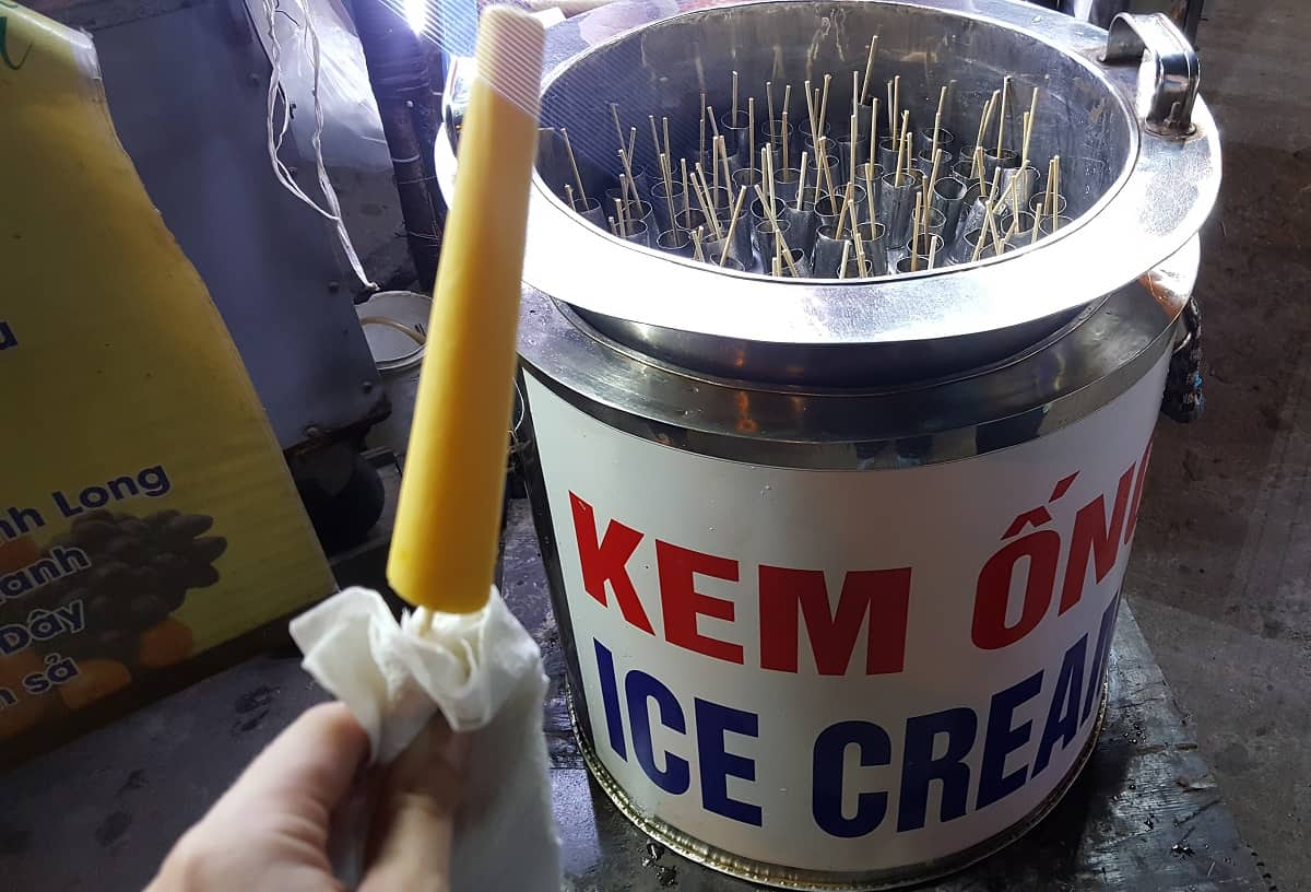 one stick of Vietnamese ice cream in front of a large container of them.