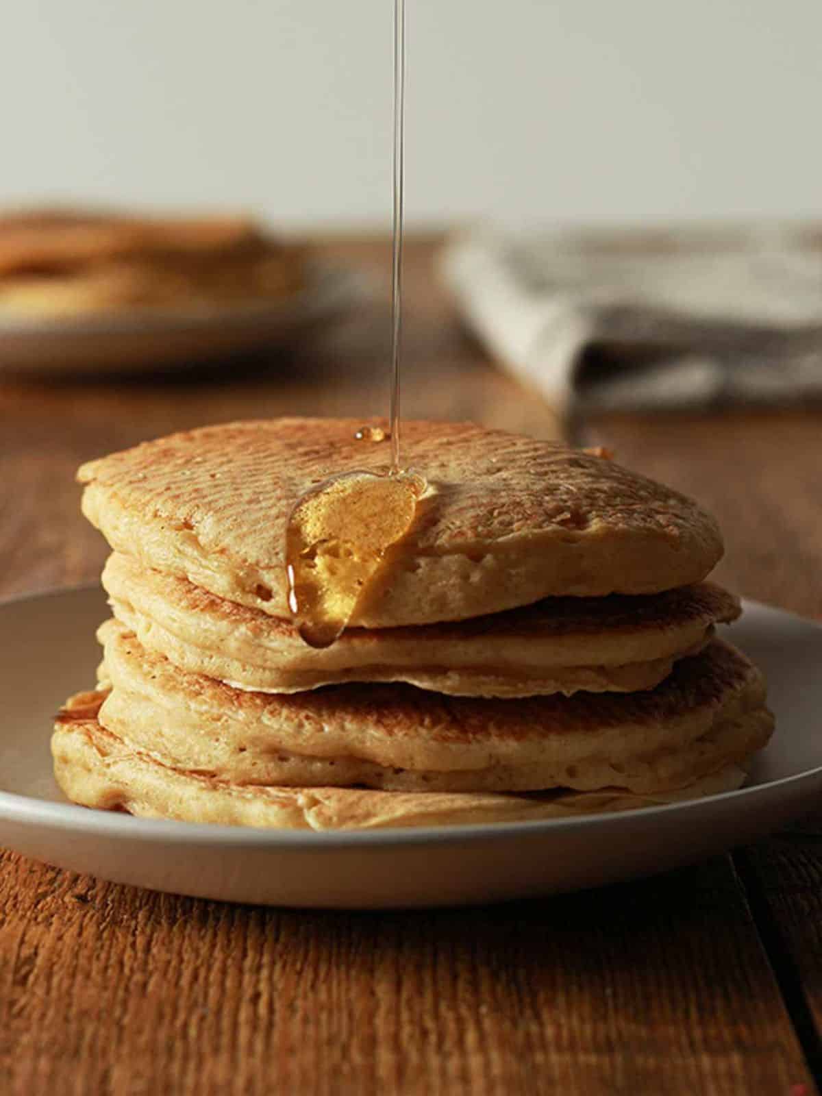 Fluffy golden vegan buttermilk pancakes stacked on a plate, drizzled with syrup.