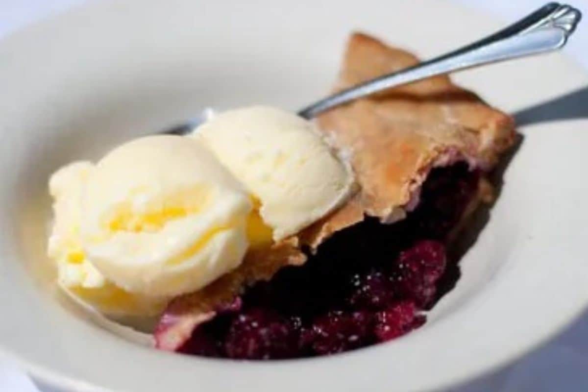 a piece of blackberry pie, topped with a scoop of creamy buttermilk sherbet, perfect for a delightful and refreshing dessert.