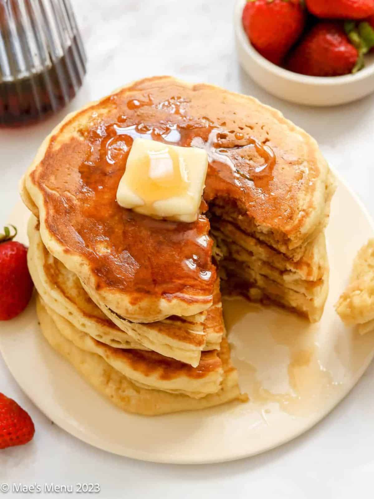 stack of golden-brown classic buttermilk pancakes topped with a pat of melting butter and drizzled with syrup.