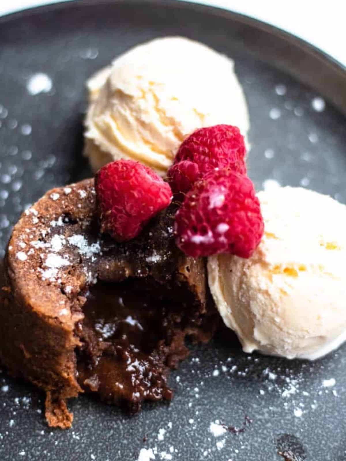 Lava cake with molten chocolate oozing out, double scoop vanilla ice cream and raspberries.
