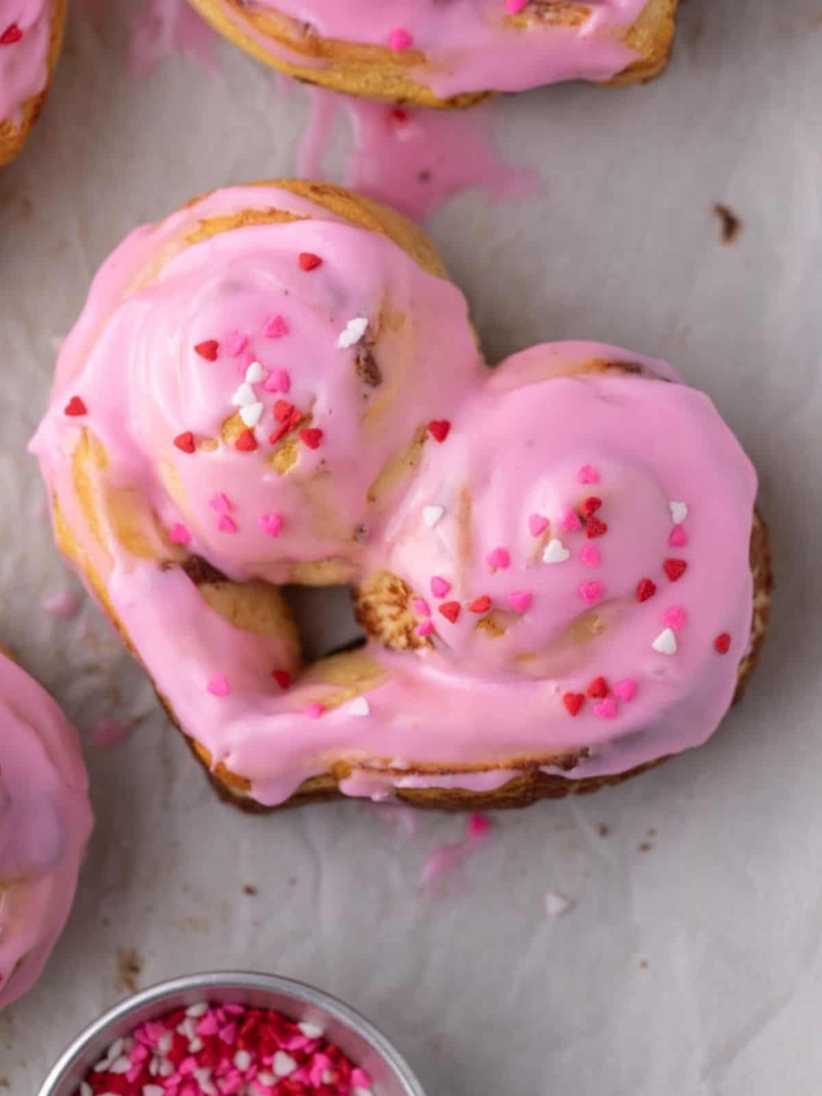 Heart-shaped Cinnamon Rolls with PInk Frosting and Candy Heart Sprinkles