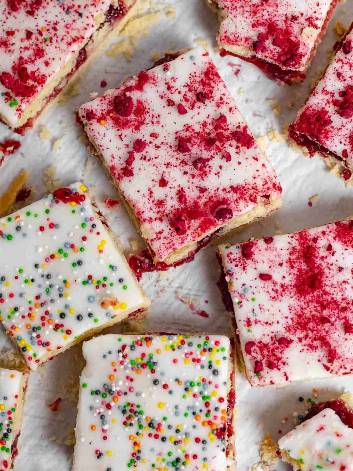 Raspberry jam filled Buttery Shorted Bread Cookie Squares with Frosting and topped with candy sprinkles and red cake crumbs