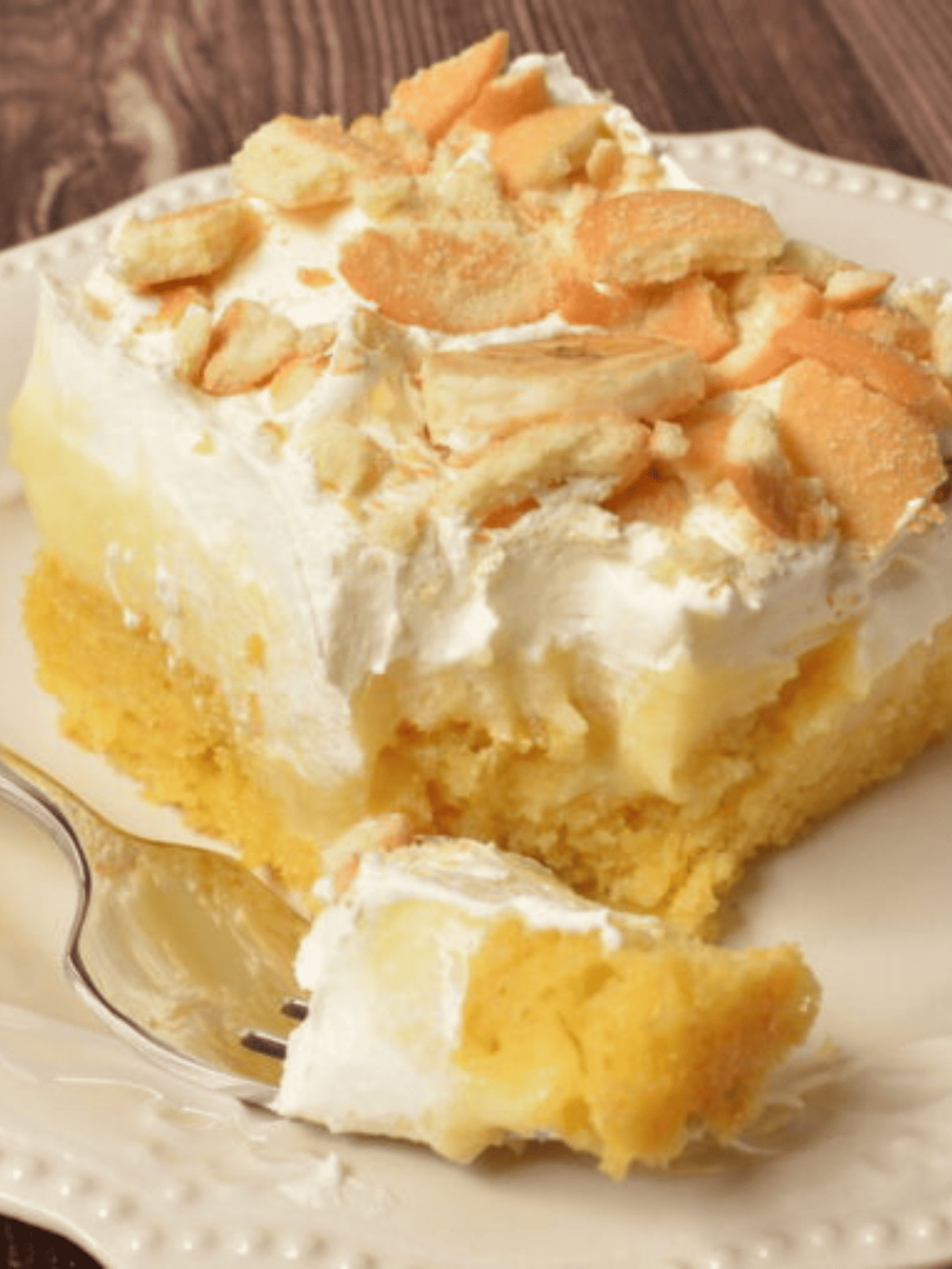 a tempting slice of banana pudding cake, adorned with layers of moist sponge, velvety pudding, and a generous topping of whipped cream and sliced bananas.