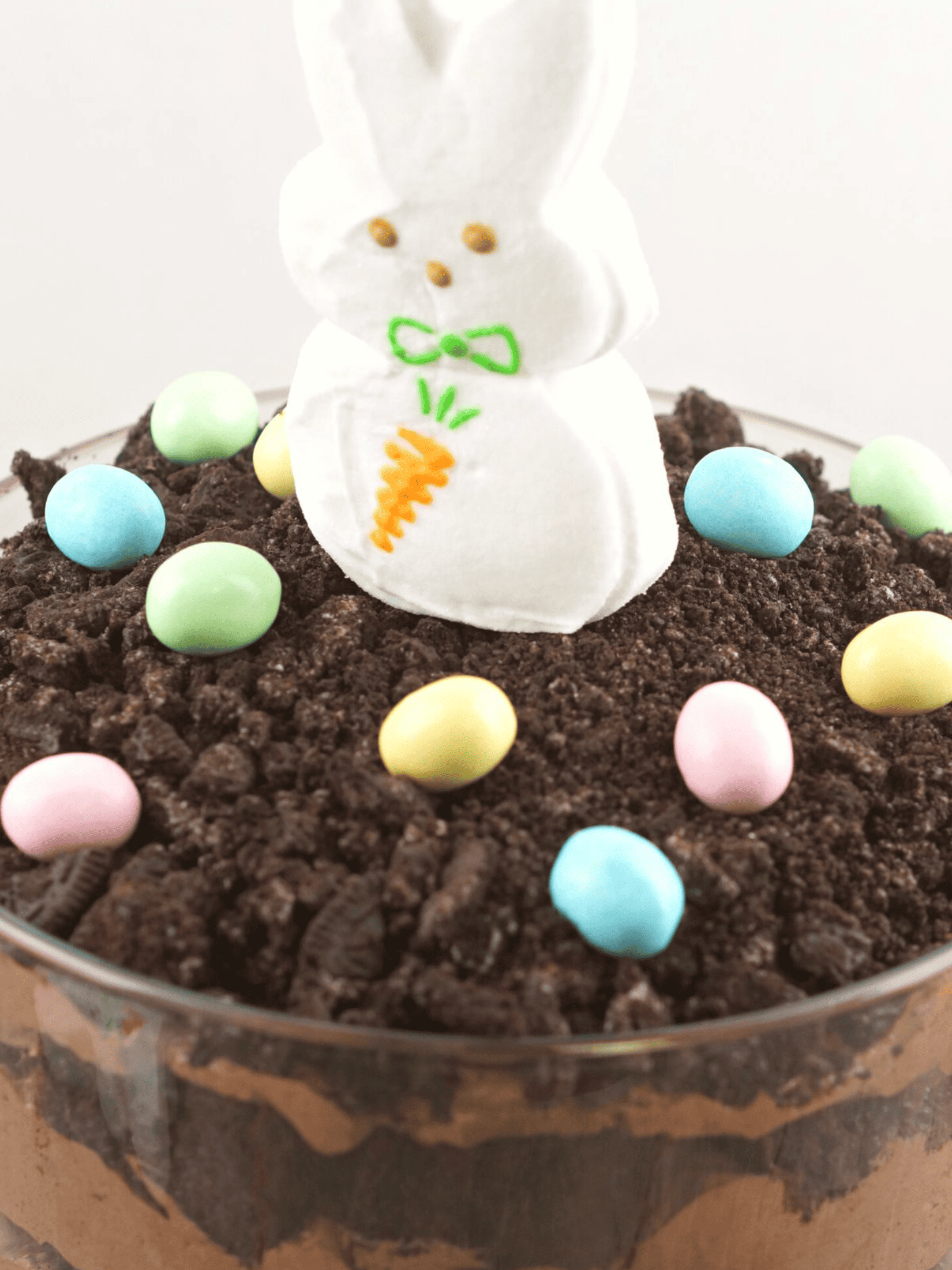 an enticing Easter Bunny Dirt Cake Trifle: layers of chocolate cake crumbles resembling soil, nestled between creamy chocolate pudding with an adorable Easter bunny-shaped cookie on top.