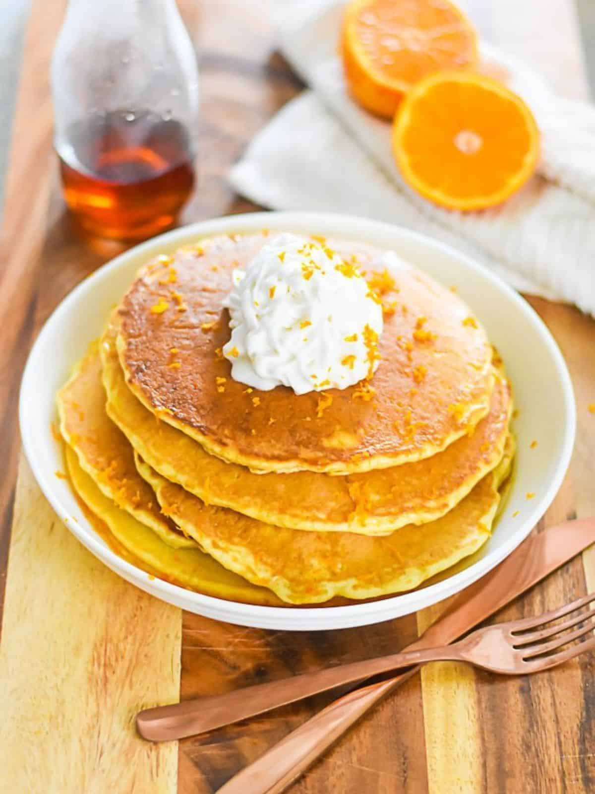 stack of fluffy Mimosa pancakes topped with whipped cream.