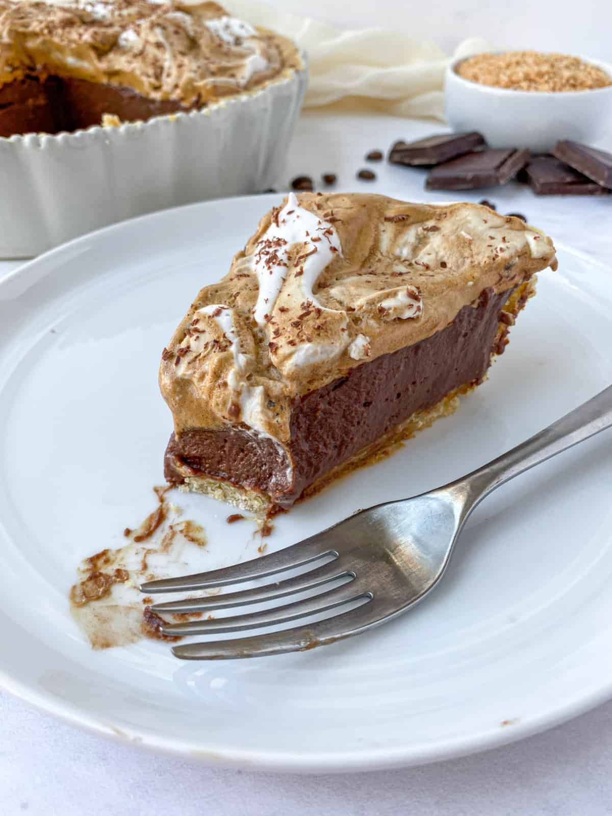 a slice of coconut mocha pie featuring a toasted coconut pastry crust filled with dark chocolate custard and topped with Dalgona coffee mixed with whipped coconut cream.