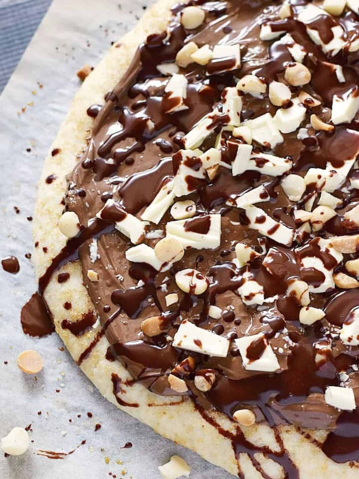 chocolate hazelnut pizza topped with white chocolate chunks, chopped hazelnuts, and a drizzle of chocolate sauce.
