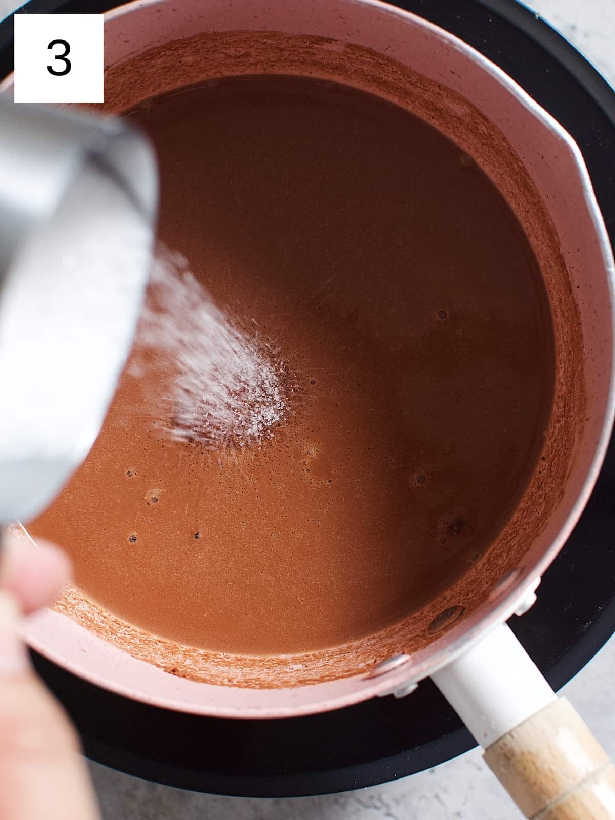 Adding granulated sugar and salt to the cocoa mixture in a heated sauce pan.