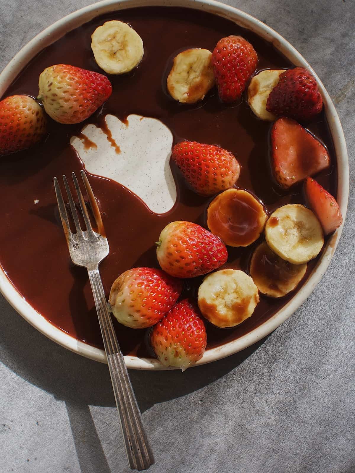 Chocolate syrup on a plate, topped with strawberries and chopped bananas.