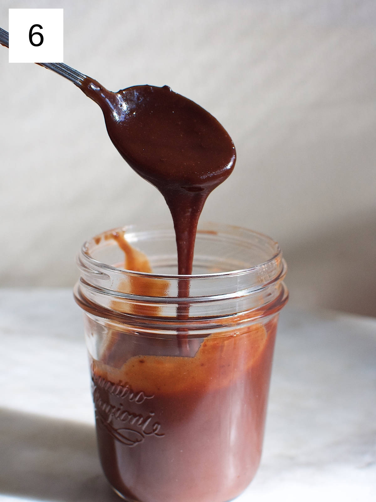 A spoon covered with fudge, drizzling on top of a glass jar filled with fudge.