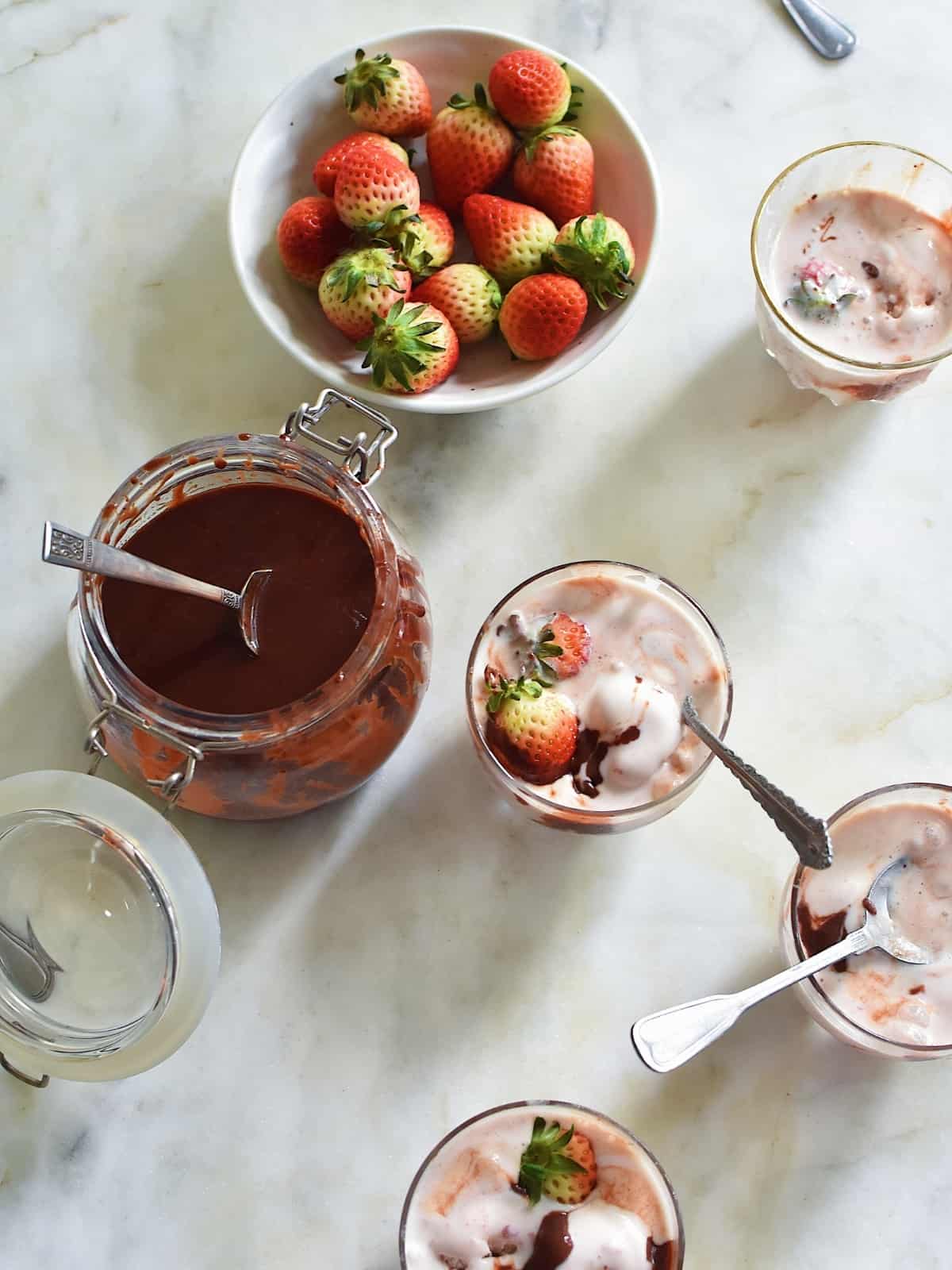 A glass jar of Hot fudge, together with a plate full of strawberries and hot fudge sundaes.