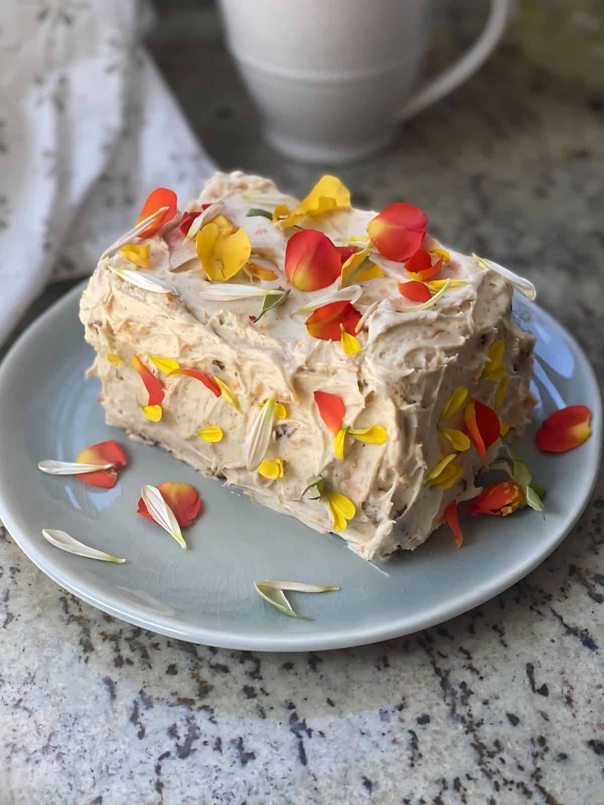 Carrot cake on a plate topped with fresh edible flowers.