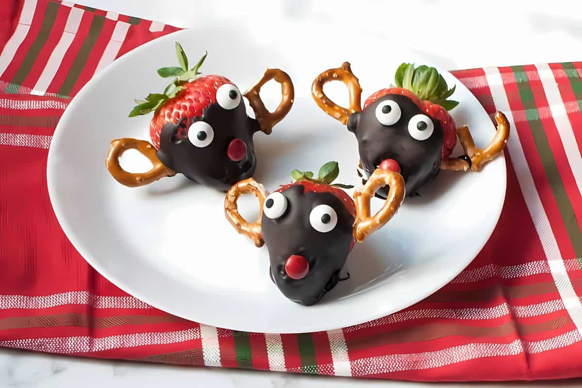 Reindeer-themed chocolate-covered strawberries on a plate, with pretzels portraying reindeer antlers.