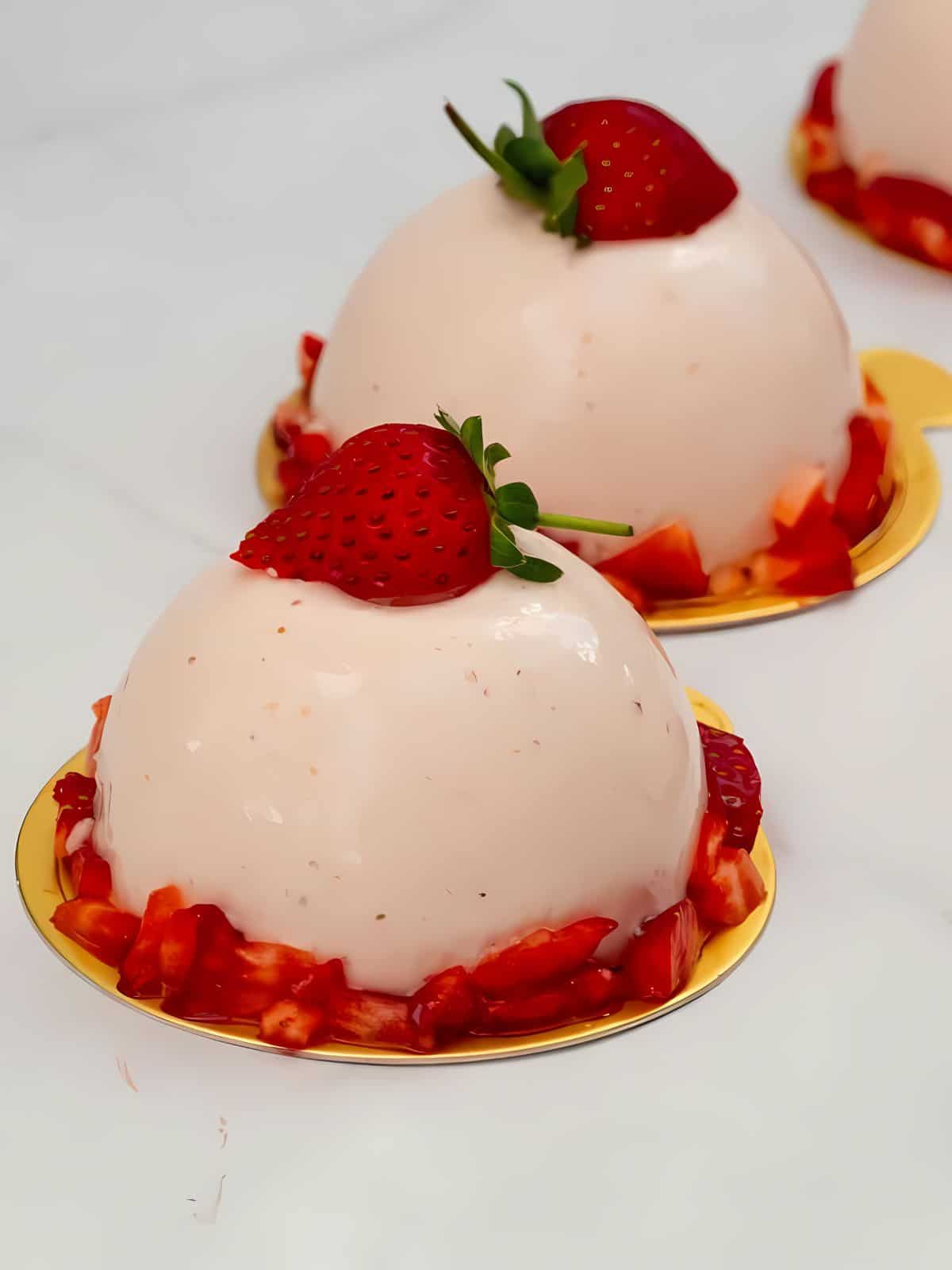 Strawberry mousse dome topped with strawberries, surrounded by small strawberry slices.
