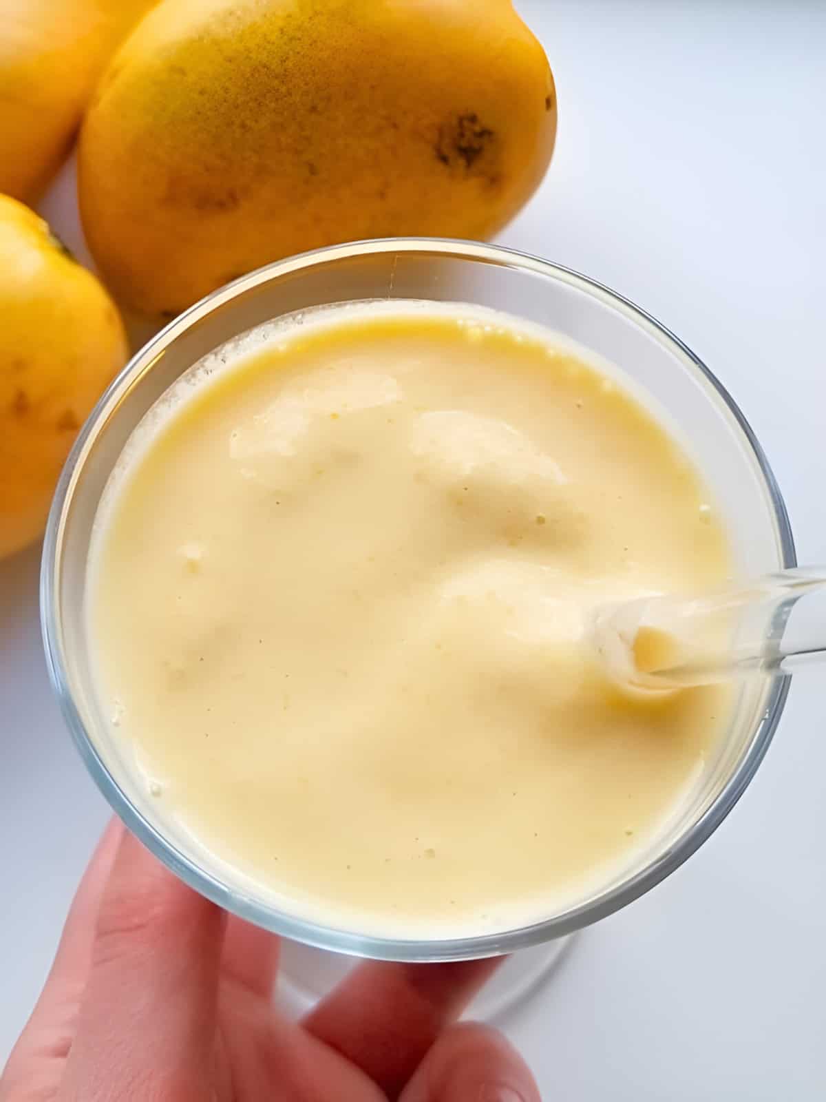Creamy mango smoothie in a glass next to fresh mangoes.