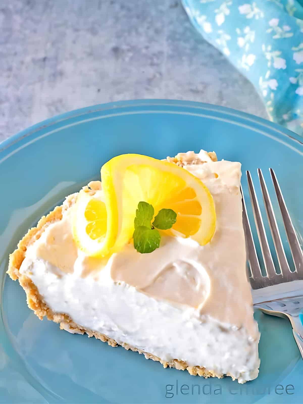 A lemonade pie topped with a swirl of cream, garnished with a slice of lemon and a sprig of fresh herb.