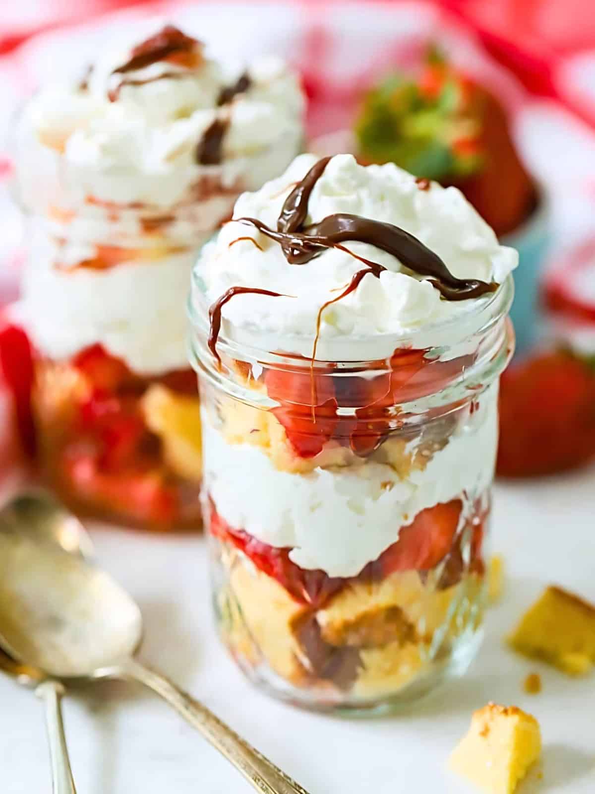 Strawberry shortcakes served in a glass jar, topped with whipped cream and drizzled with chocolate syrup.