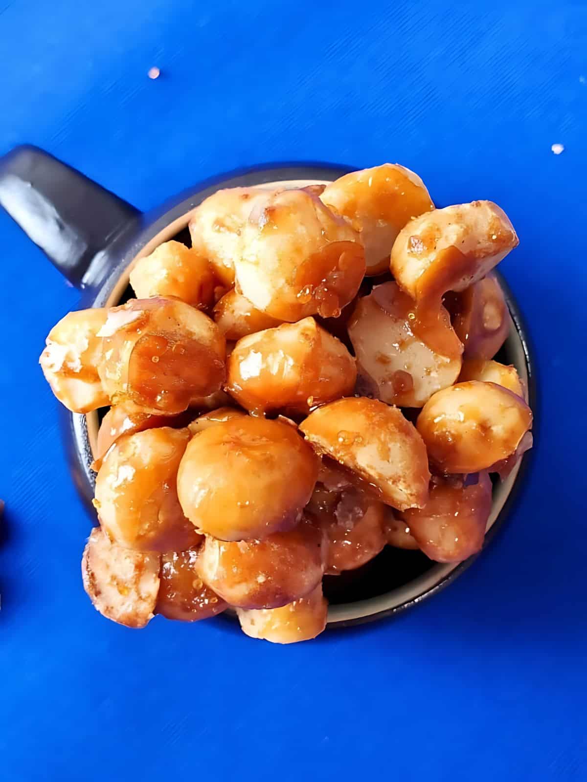 Caramelized candied macadamia nuts places in a mug.