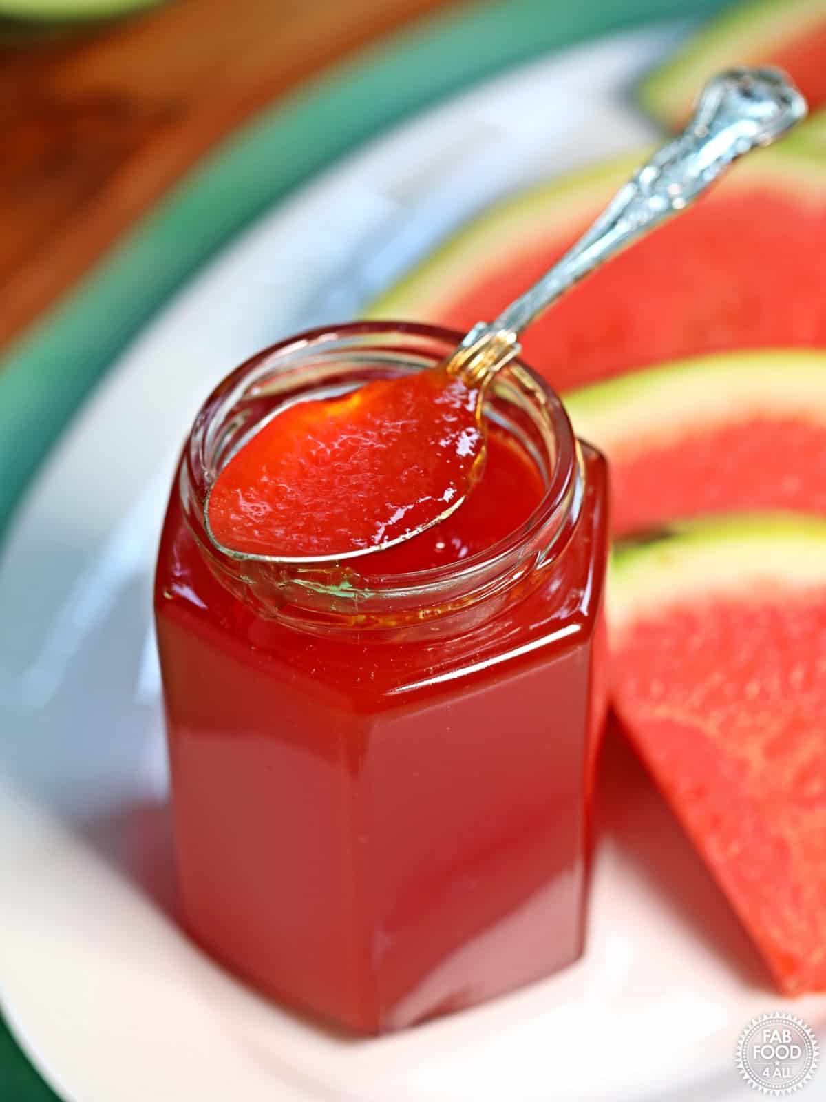 A spoonful of watermelon jam from a glass jar.