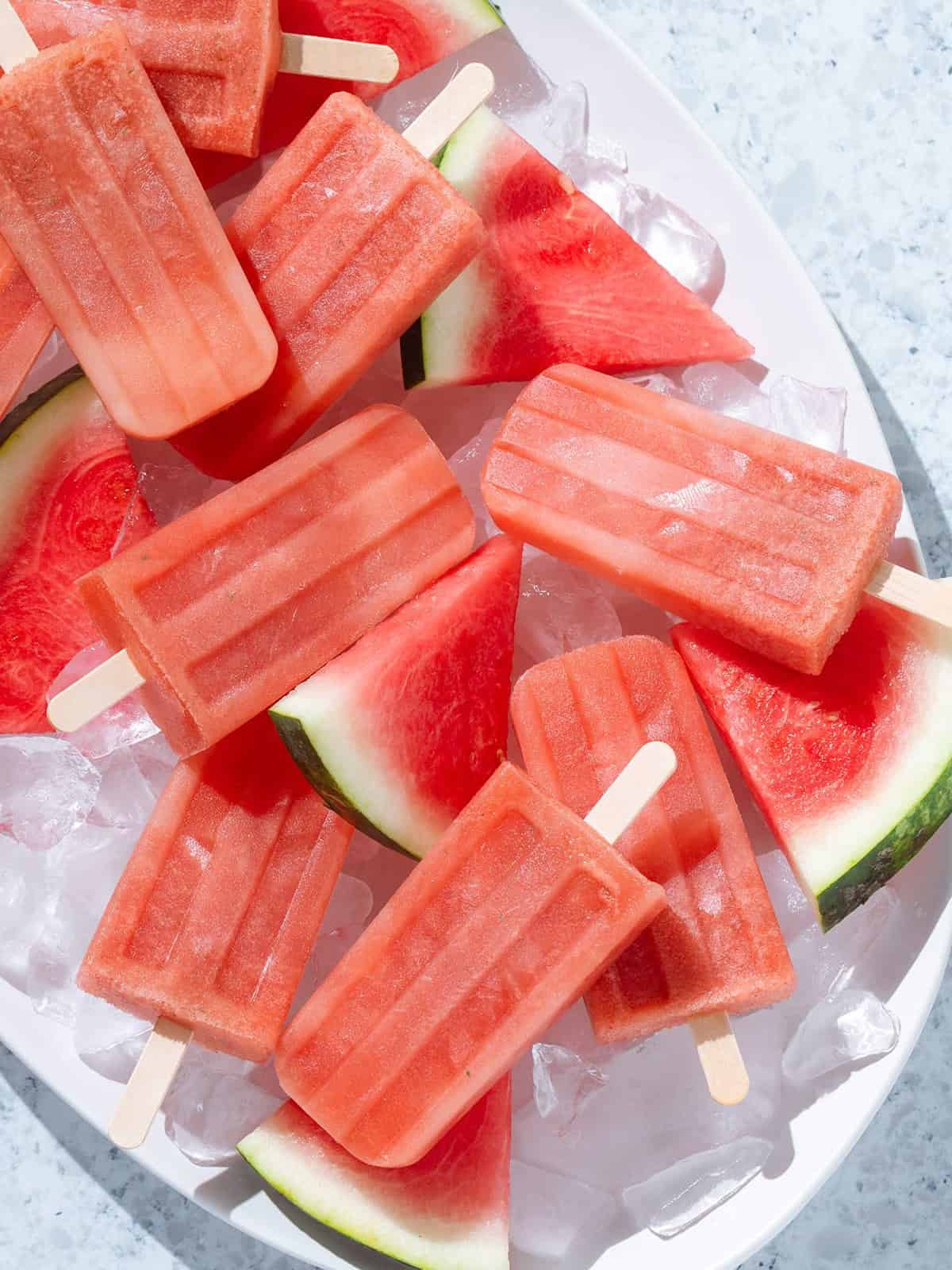 Watermelon popsicles on a plate full of ice cubes.