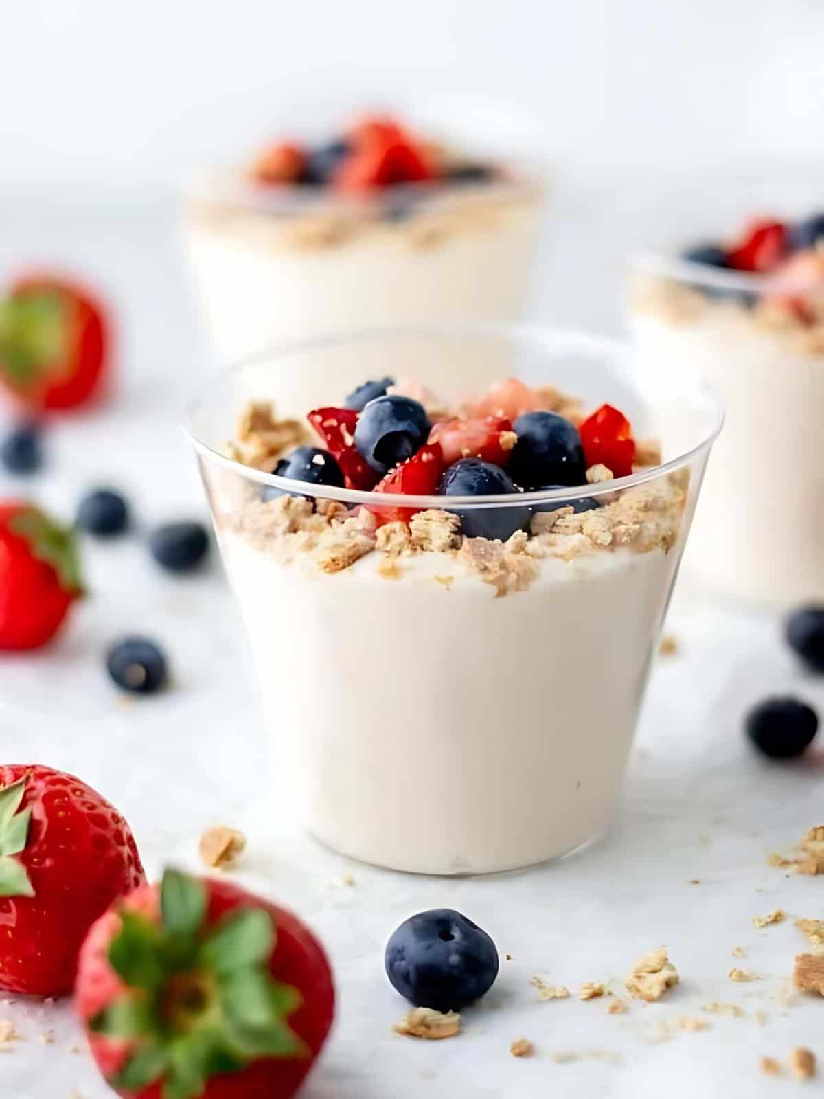 A serving of cheesecake cups topped with berries and crumbles in a small cup.