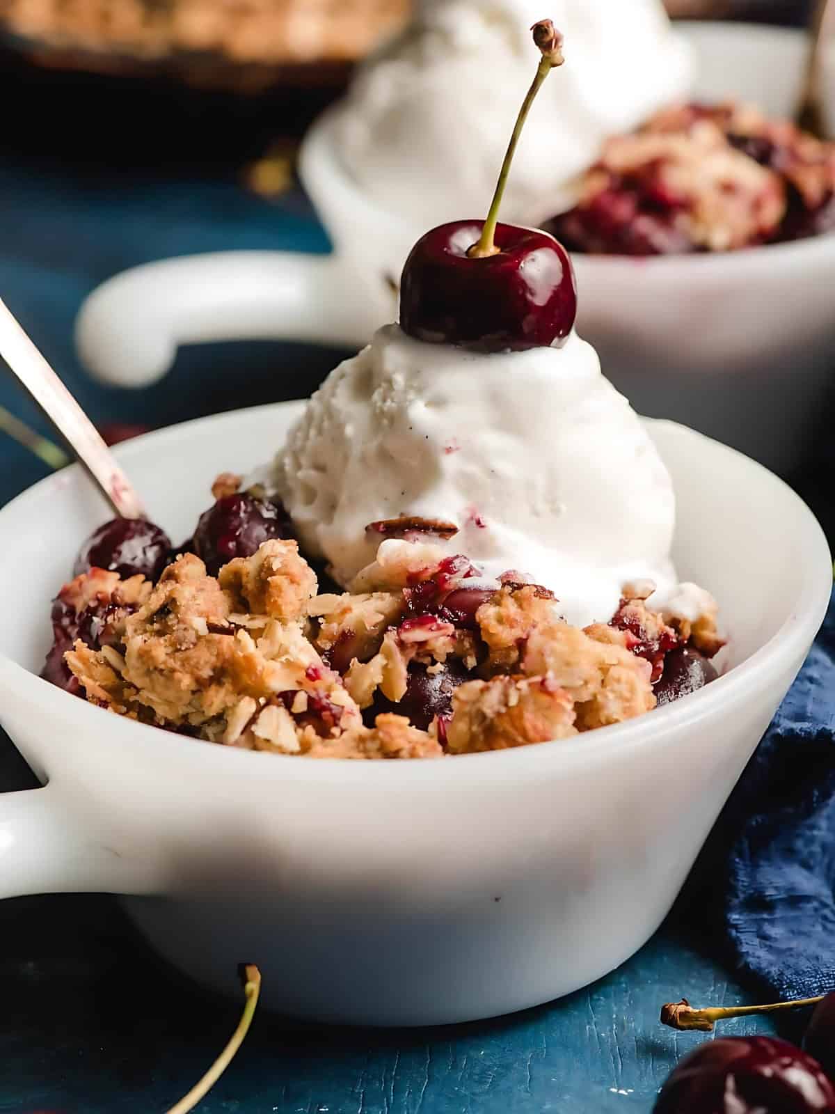 A serving of cherry almond crumble topped with cherry on top and cream.