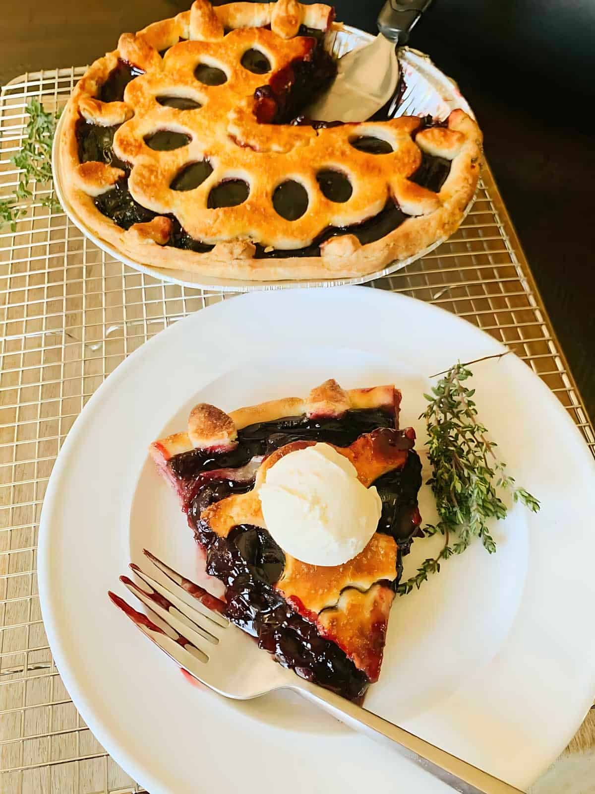 A whole cherry pie next to a slice of cherry pie on a plate, topped with cream cheese.