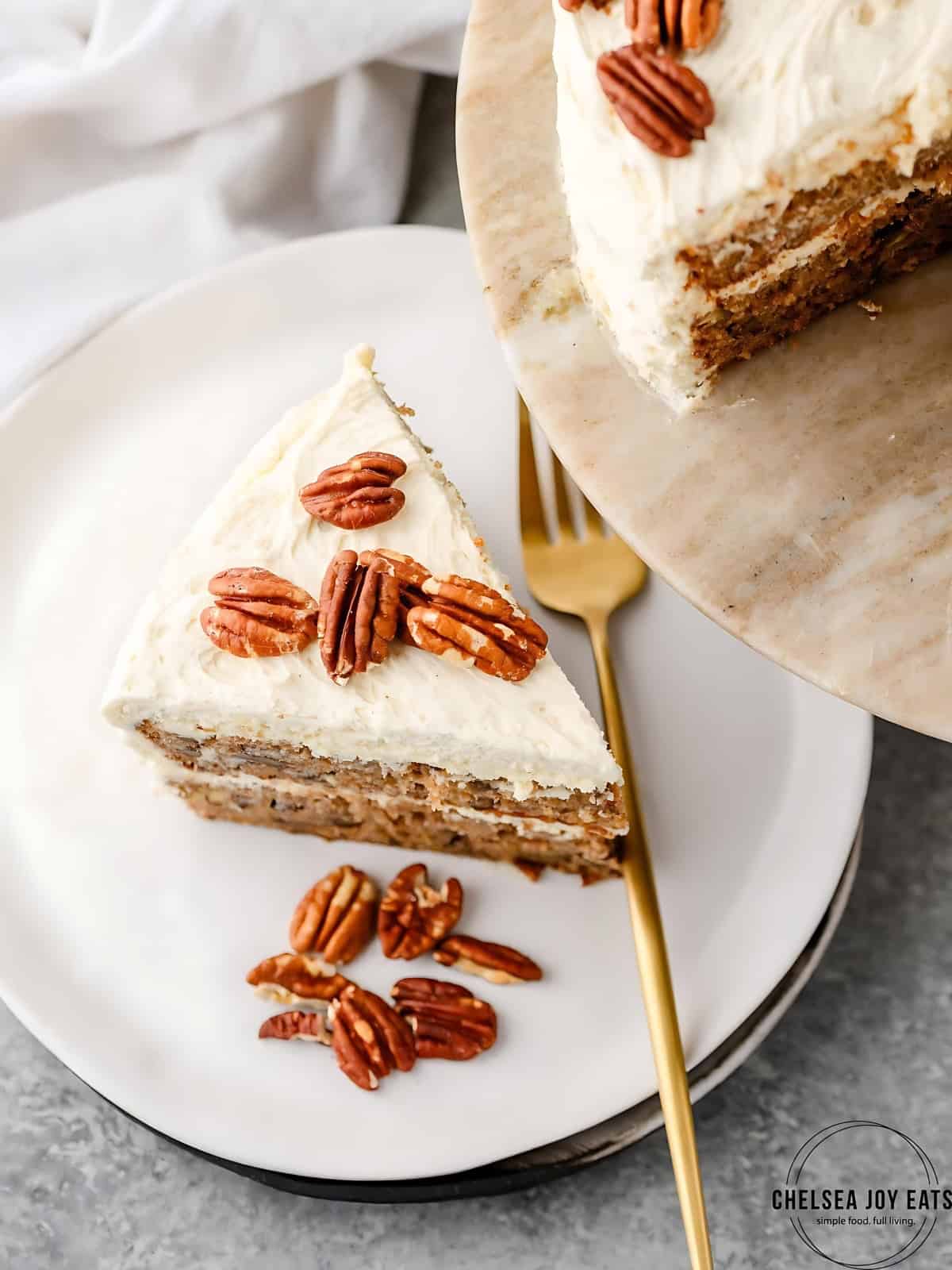A serving of Hummingbird Cake on a plate with toasted pecans on top.