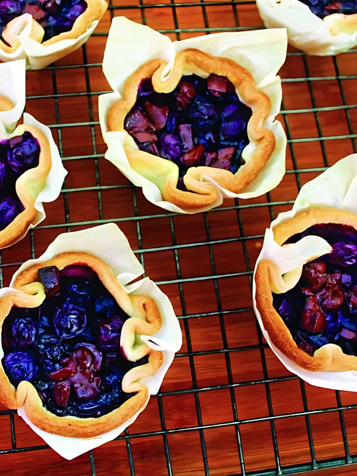 Mini blueberry and chocolate tarts fresh out of the oven on a grilled baking tray.
