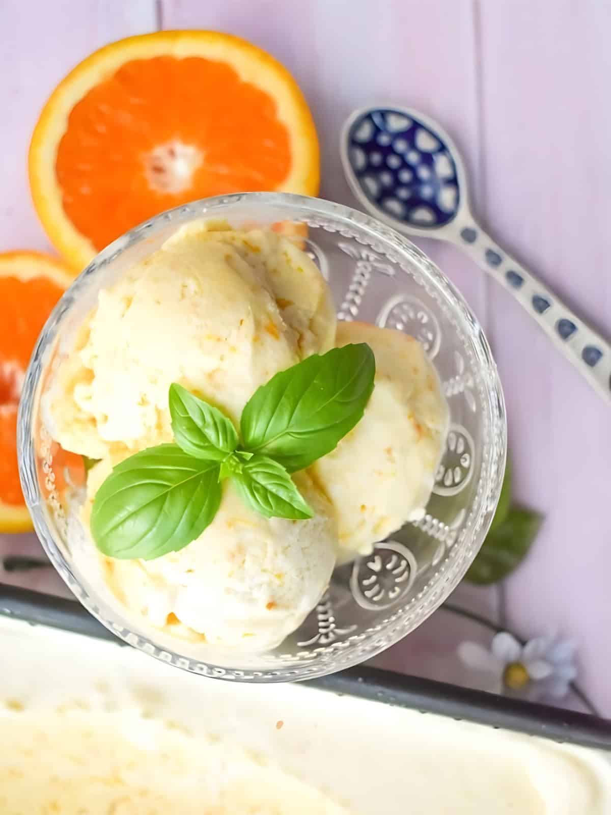Orange ice cream topped with fresh basil on top, next to a sliced orange.