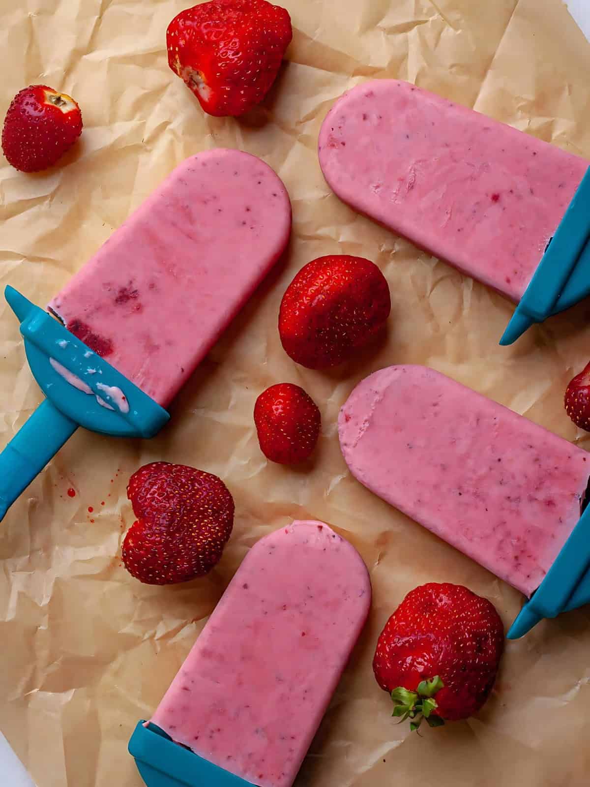 Homemade strawberries and cream Popsicles next to strawberries.