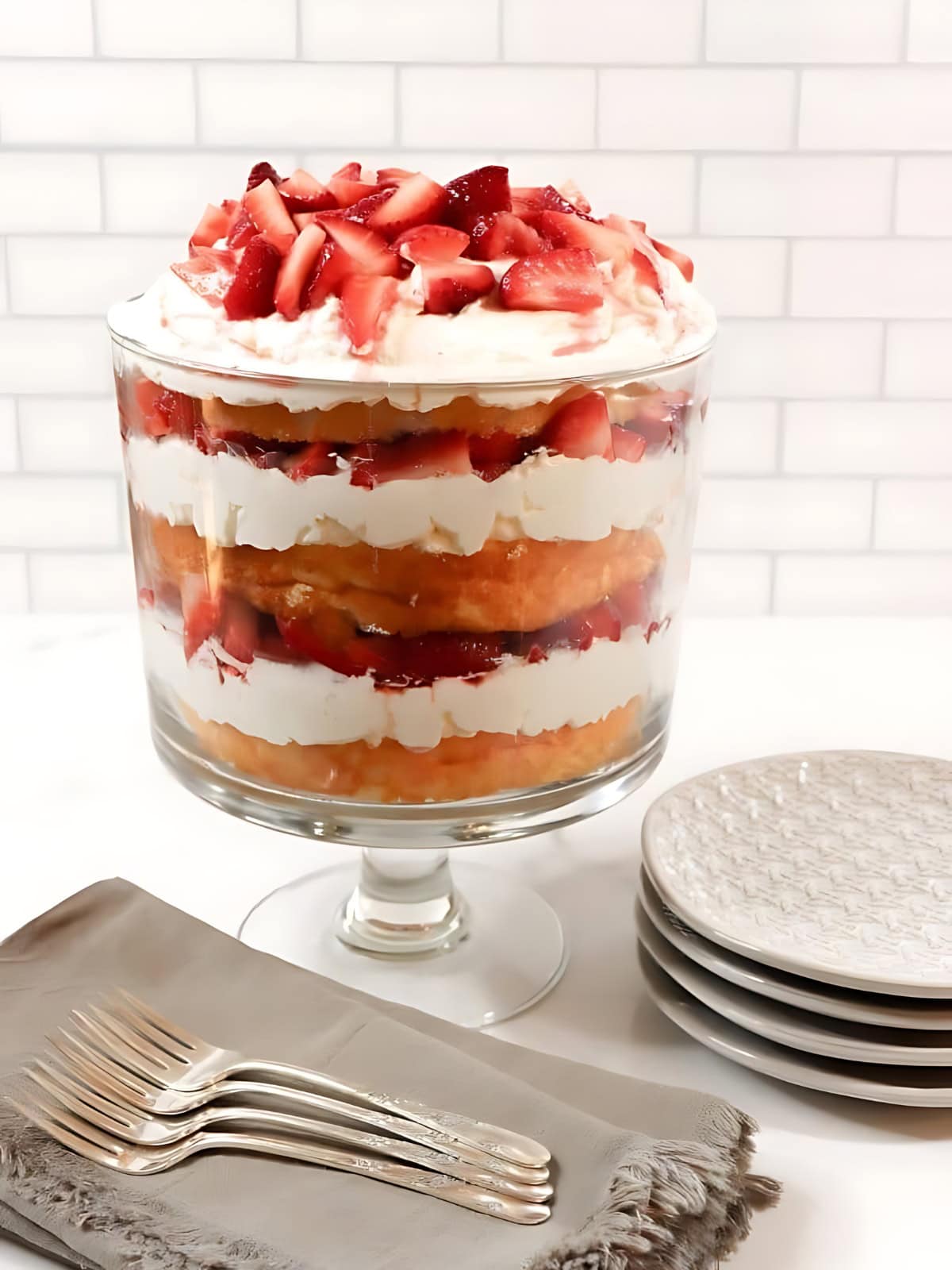 Strawberry Angelfood Cake Trifle topped with sliced strawberries, placed on a table next to a set of forks and plates.