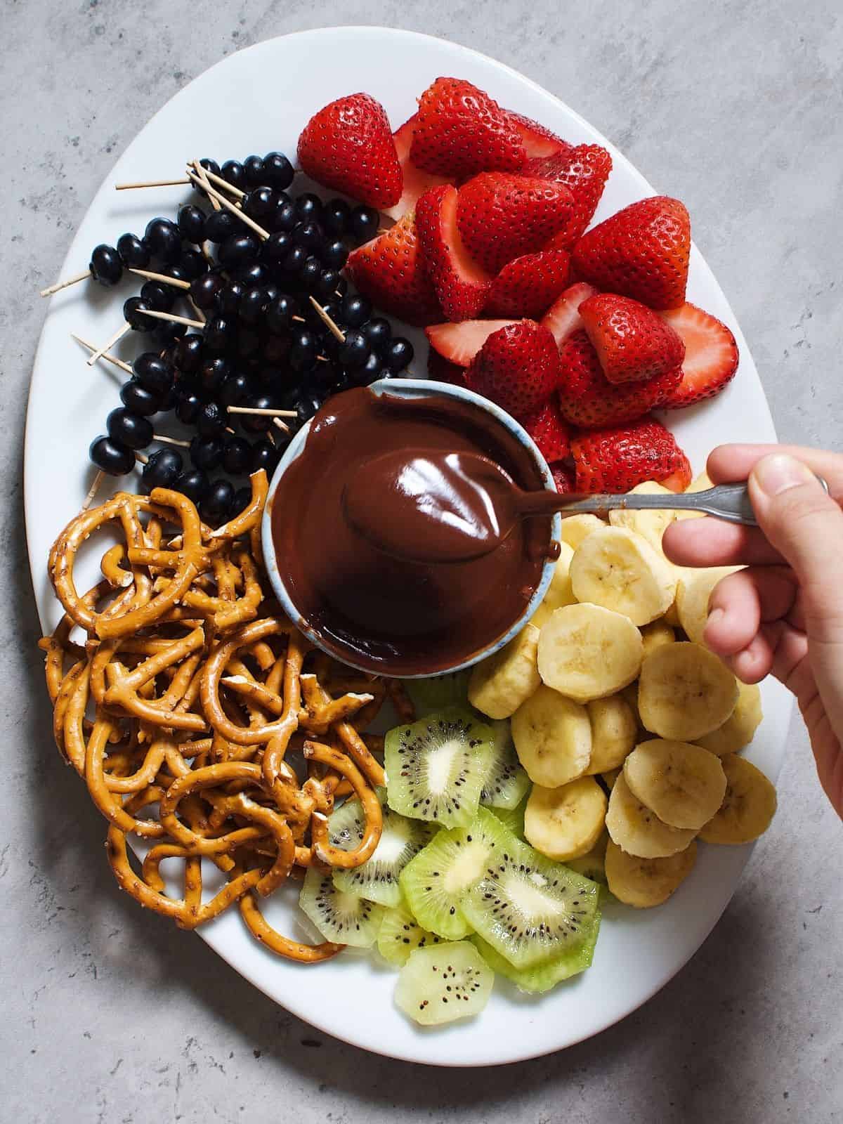 chocolate dipping sauce on a platter with fruit and pretzels.