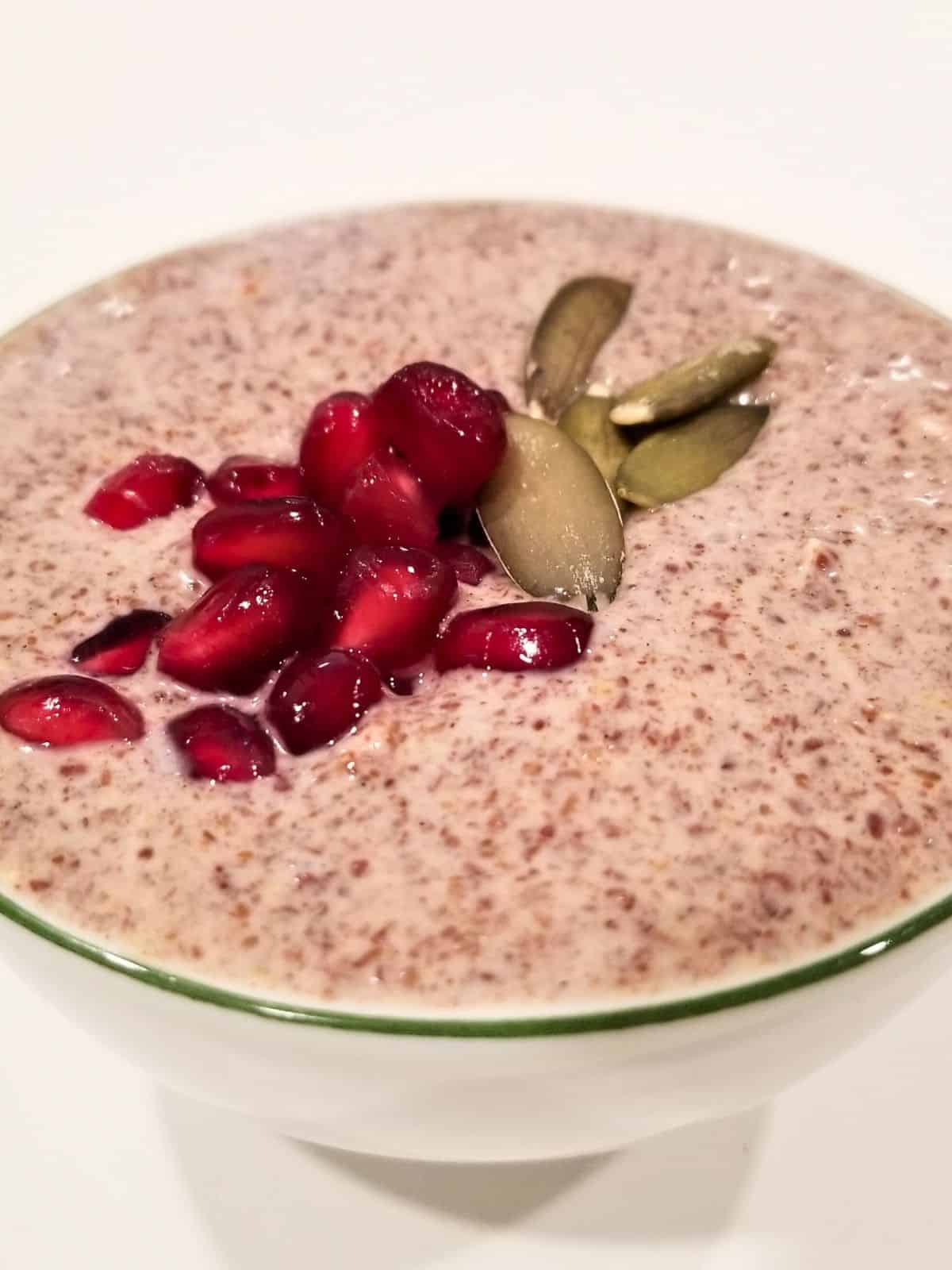 small white bowl of flax seed pudding topped with pomegranate seeds and pumpkin seeds.
