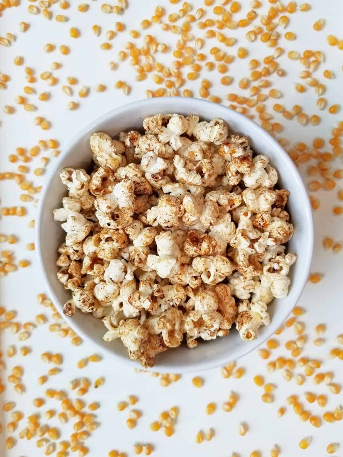 white bowl of kettle corn on a white background with unpopped kernels surrounding it.