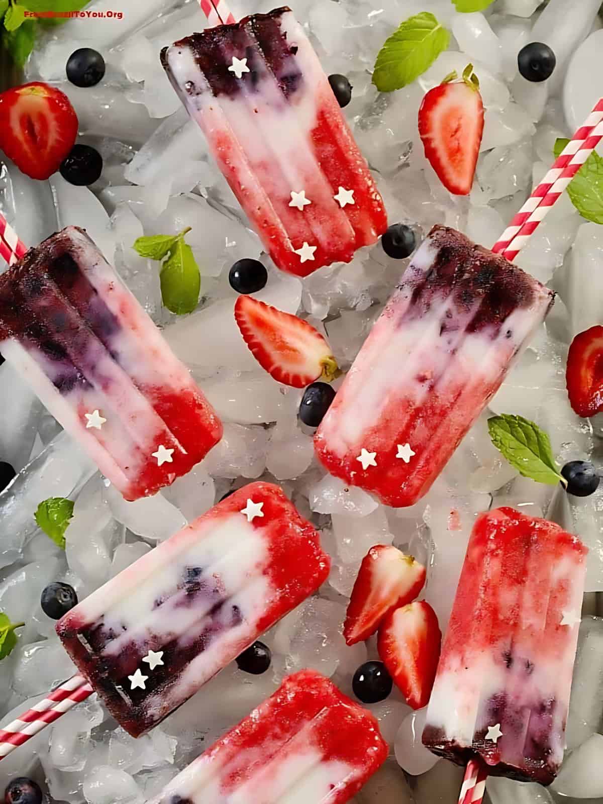Berry yogurt popsicles resting on ice cubes next to strawberries and blue berries..