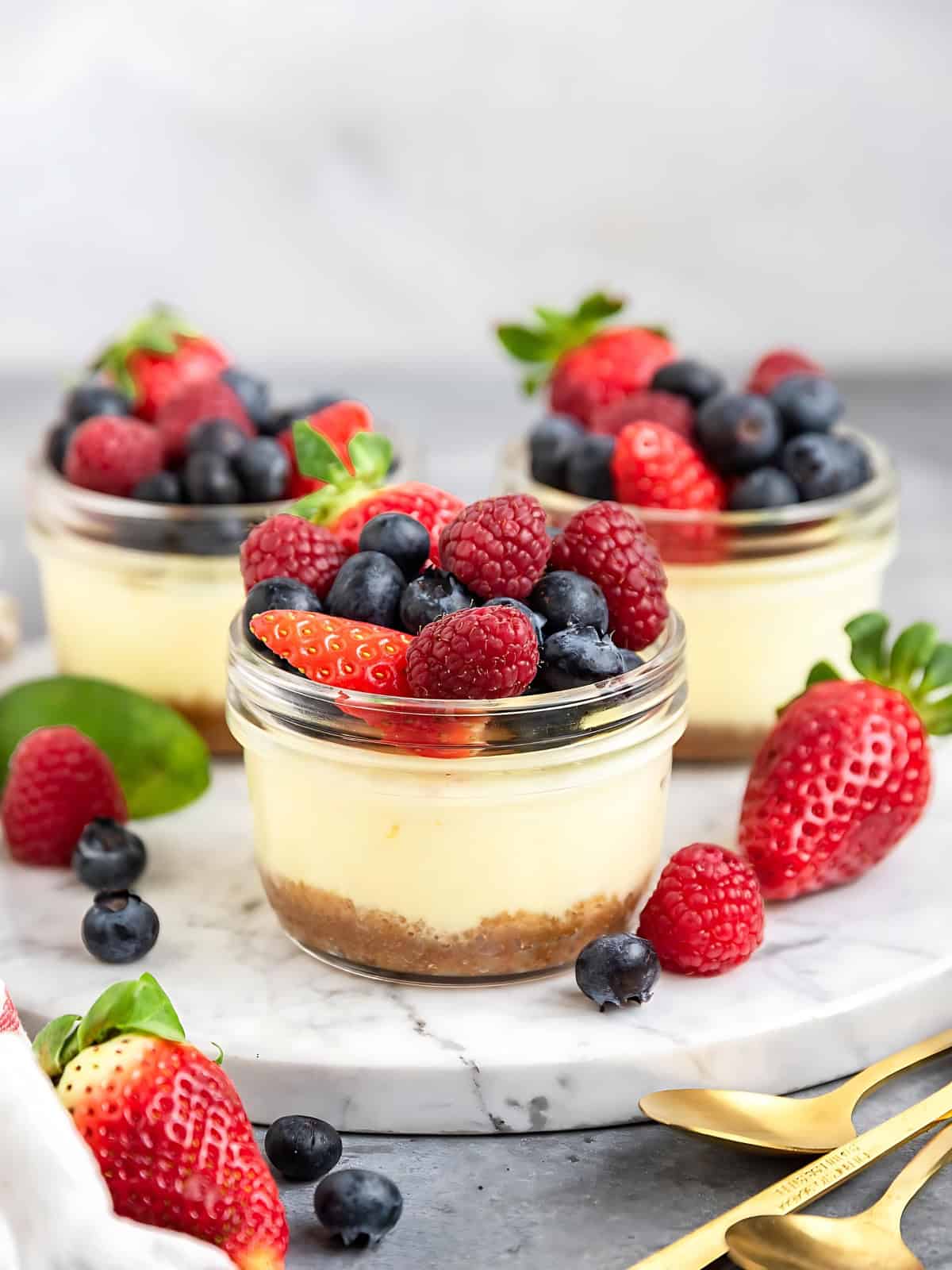 Pot mini cheese cakes in a small glass cup topped with strawberries, blueberries, and raspberries.