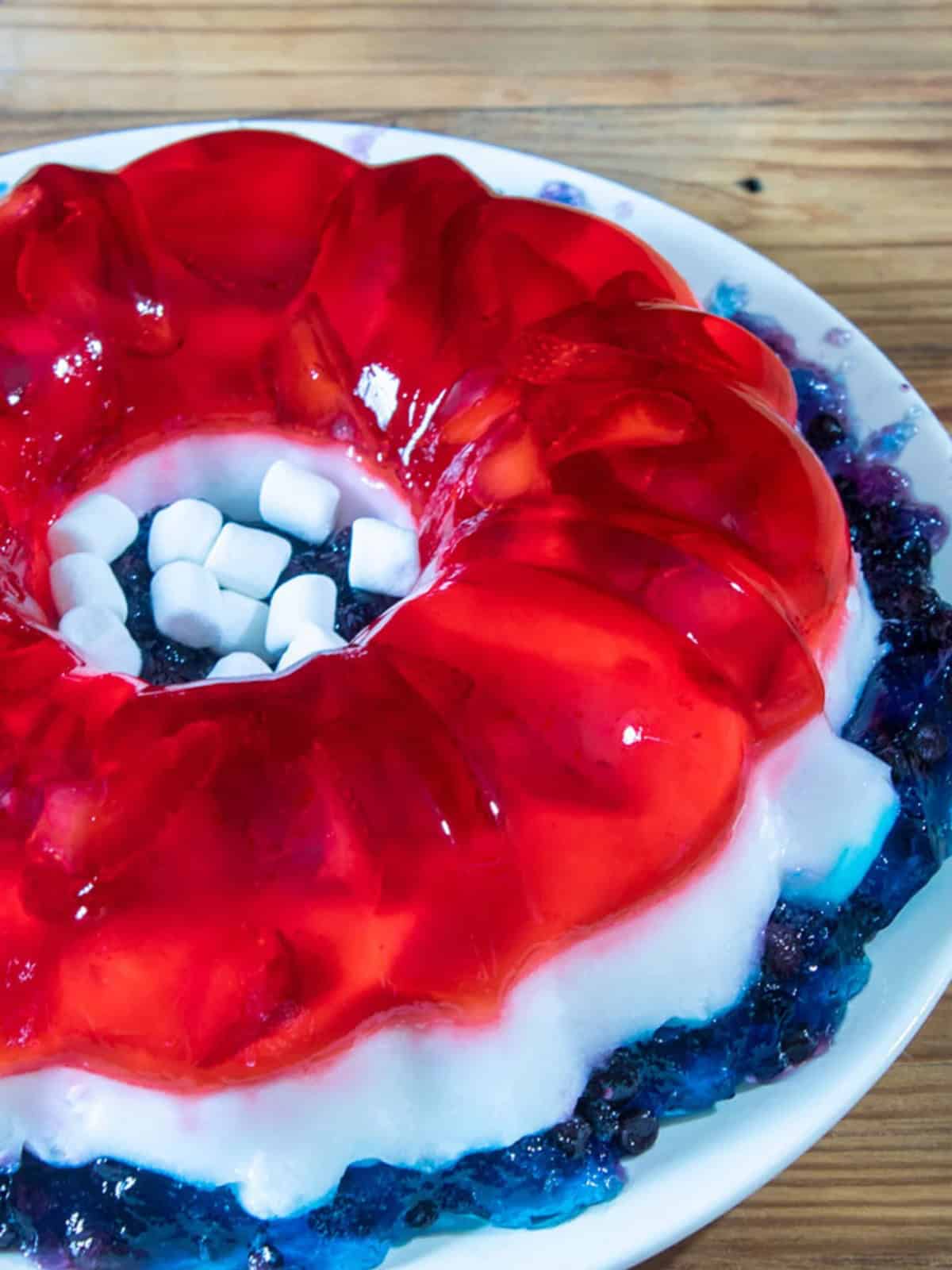 Jello salad mold in a plate with marshmallows in the center.
