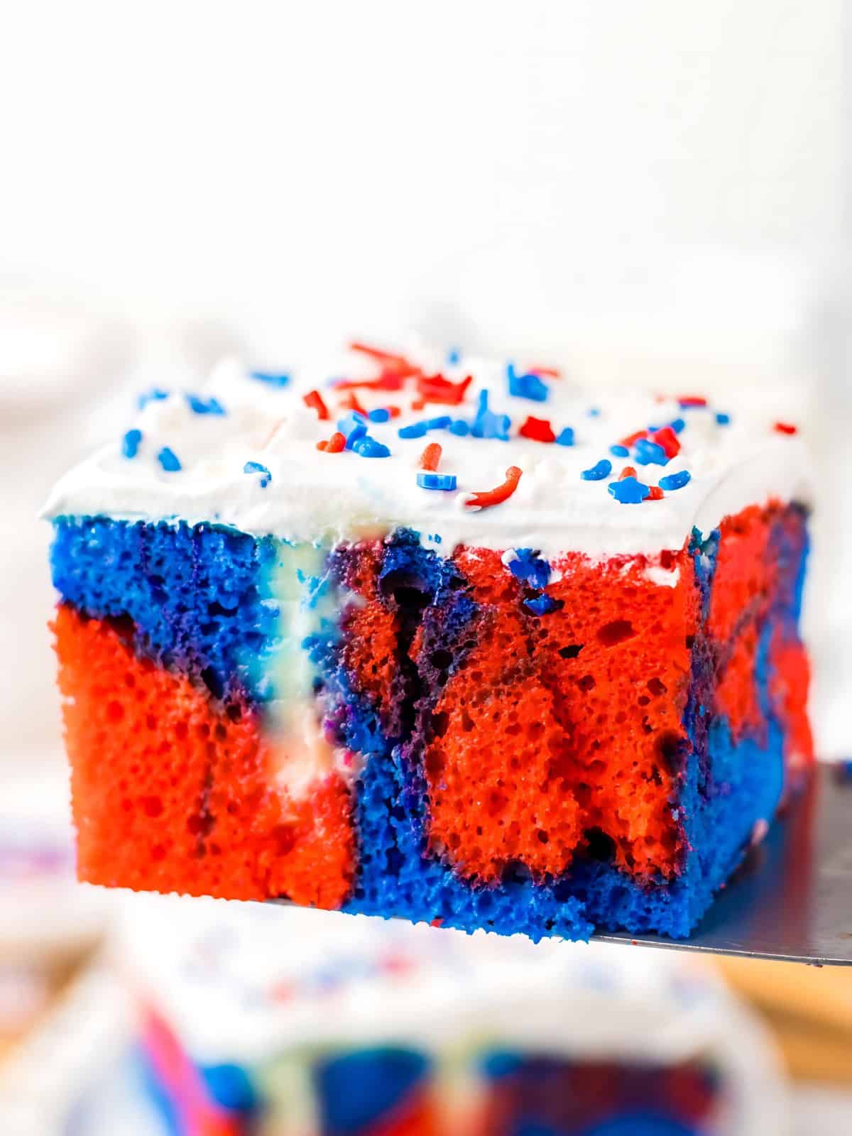 Red white and blue colored poke cake with sprinkles.