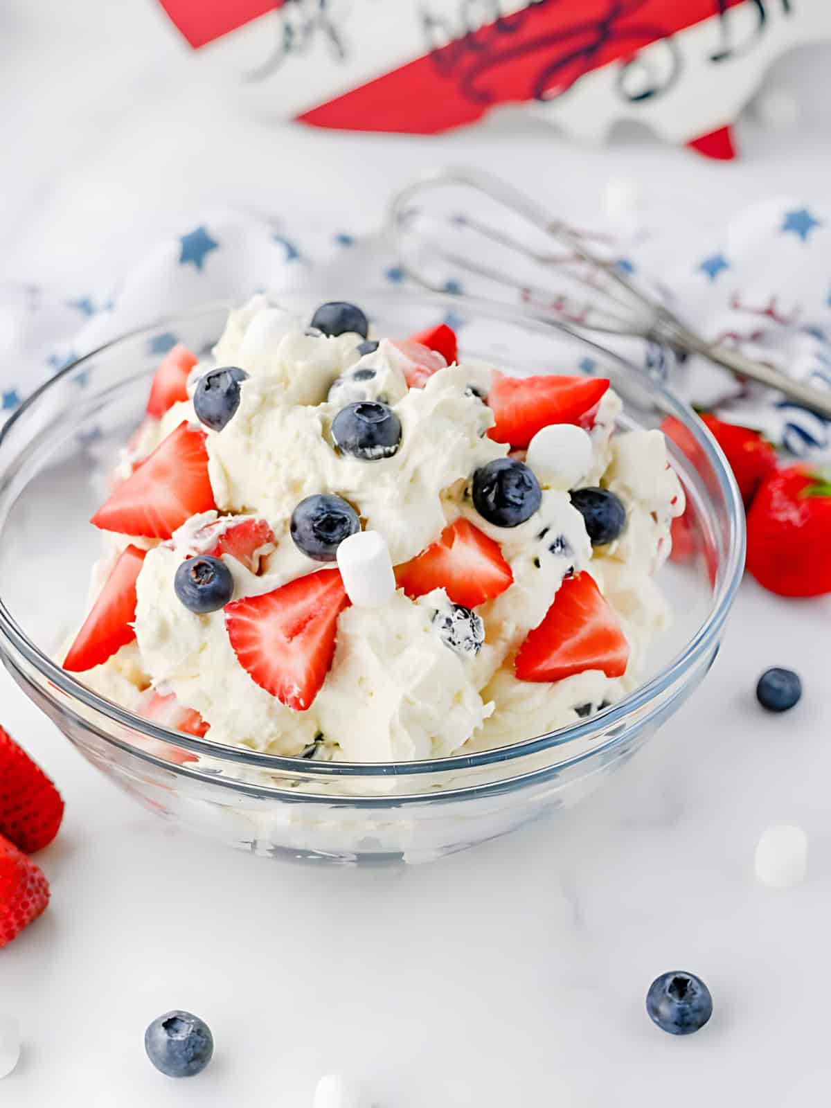 Red white and blue cheesecake salad in a bowl topped with strawberries. and blueberries.