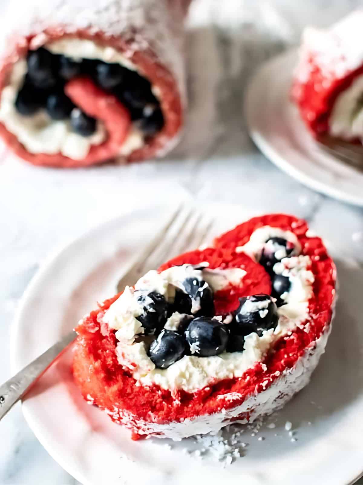 A slice of red white and blue roulade with blueberry filling in a plate.