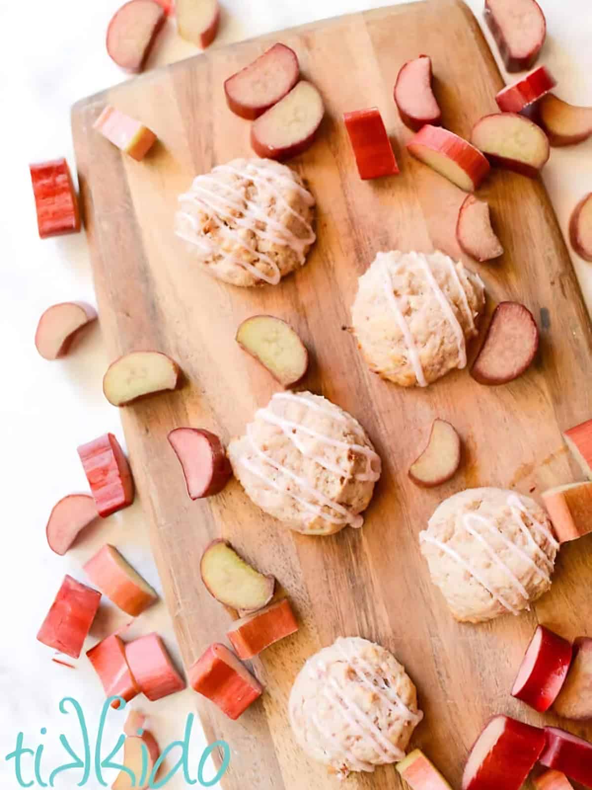 Rhubarb cookies on a wooden board next to slices of rhubarb.