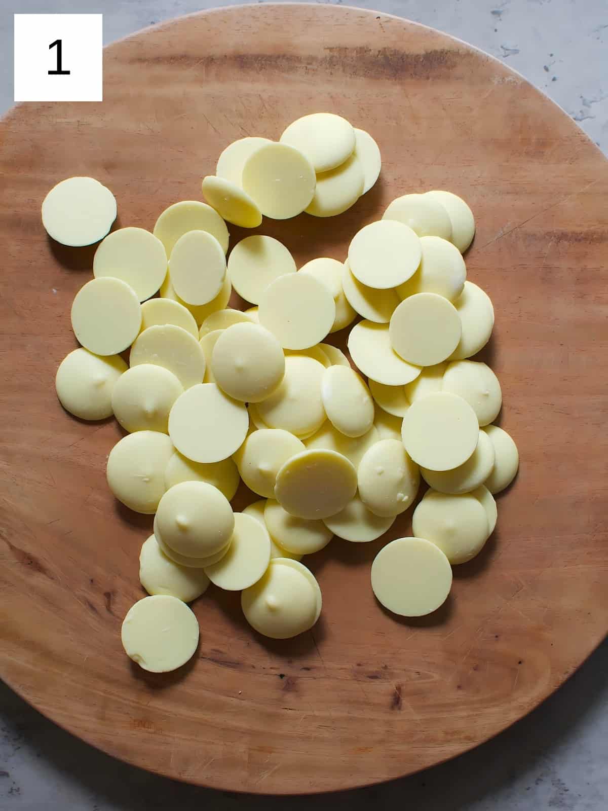 A bunch of disk shaped white chocolates on a wooden board.